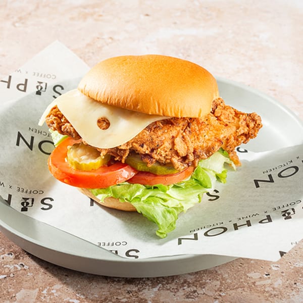 Crispy fried chicken sandwich with cheese, lettuce, tomato, and pickles on a bun.
