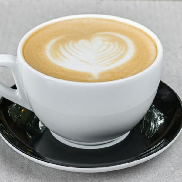 Close-up of a white coffee cup with latte art in the shape of a heart on a black saucer.