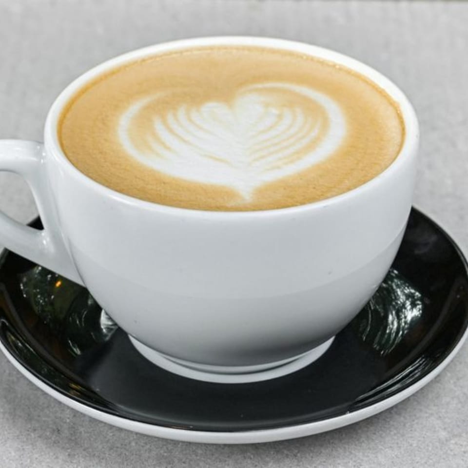 Close-up of a white coffee cup with latte art in the shape of a heart on a black saucer.