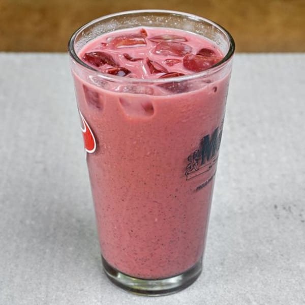 A tall glass of pink smoothie with ice and fruit chunks, featuring a logo on the side.