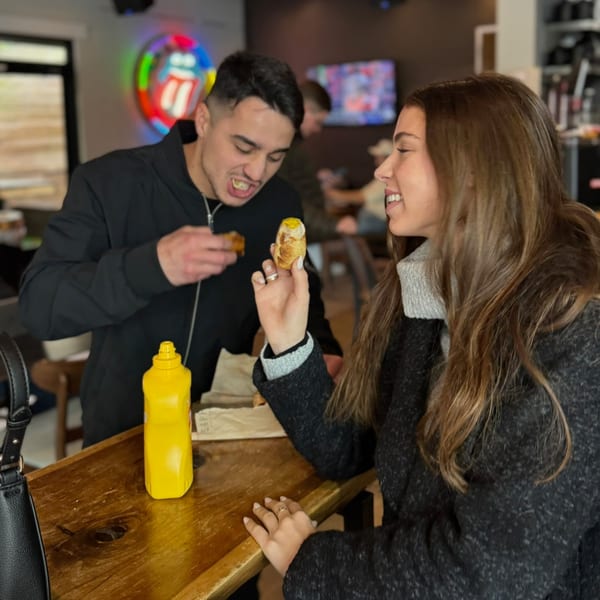 Two young adults enjoying hot dogs with mustard at a casual restaurant.