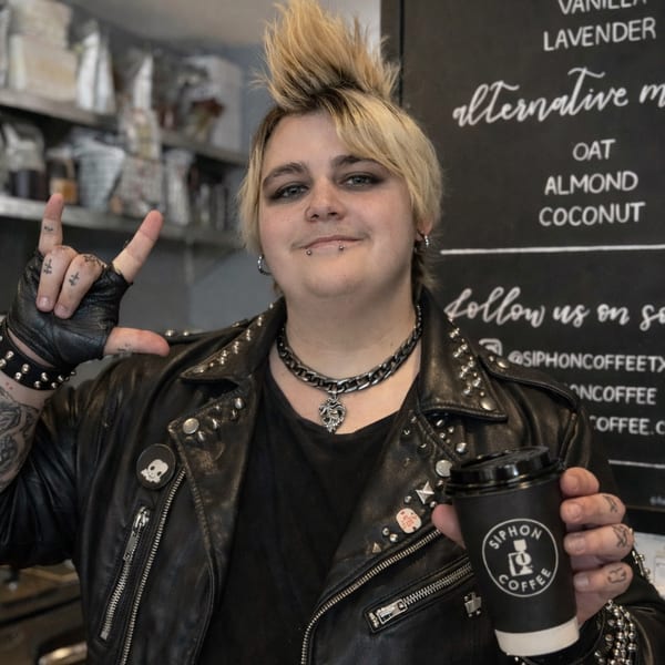 A person in a studded leather jacket and punk hairstyle holds a Siphon Coffee cup, making a rock-on gesture.