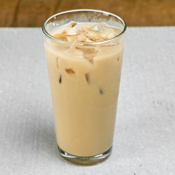 Iced coffee with milk and ice cubes in a clear glass on a light gray surface.
