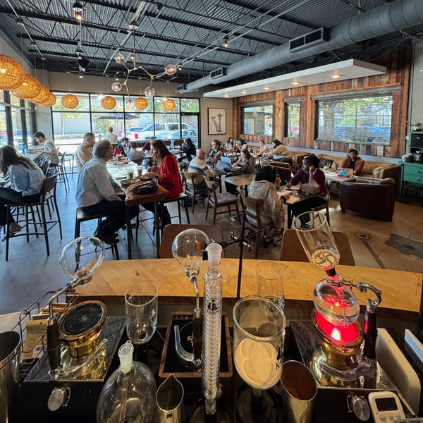 A bustling coffee shop interior with customers working and socializing, featuring unique brewing equipment in the foreground.