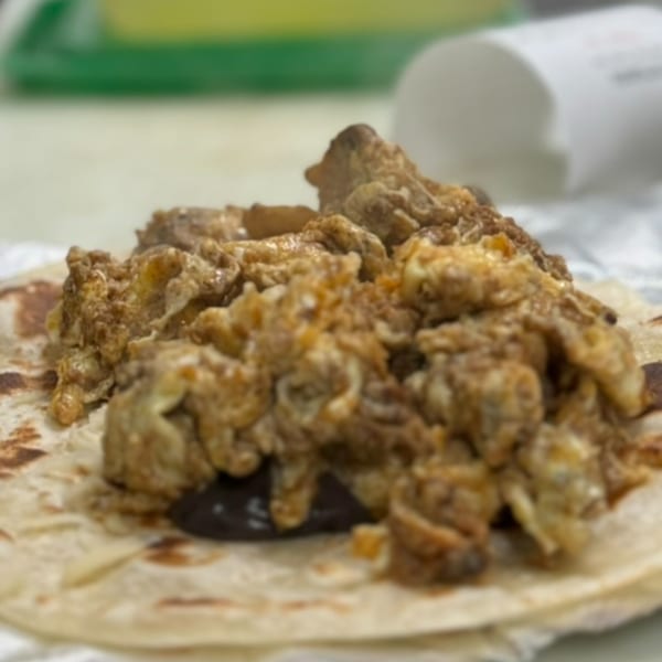 Close-up of a taco with scrambled eggs and dark filling on a tortilla.