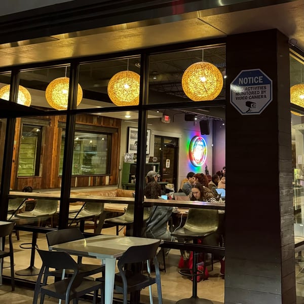 A modern cafe interior with warm lighting, visible through large glass windows, showing patrons working on laptops.