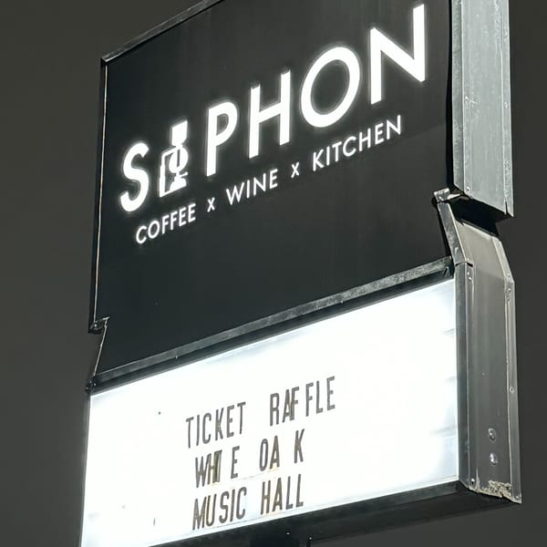 A black and white sign for "SIPHON COFFEE x WINE x KITCHEN" with "TICKET RAFFLE WHITE OAK MUSIC HALL" below.