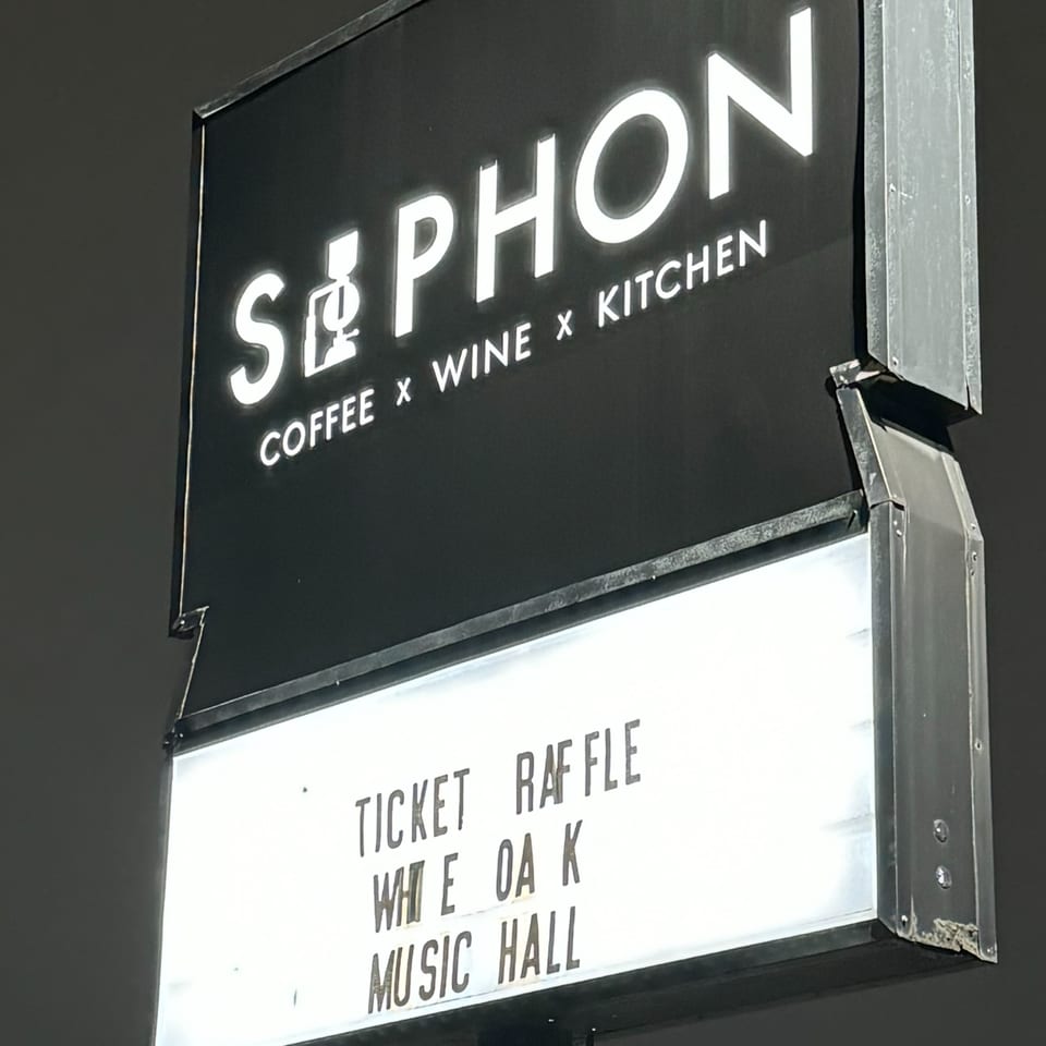 A black and white sign for "SIPHON COFFEE x WINE x KITCHEN" with "TICKET RAFFLE WHITE OAK MUSIC HALL" below.