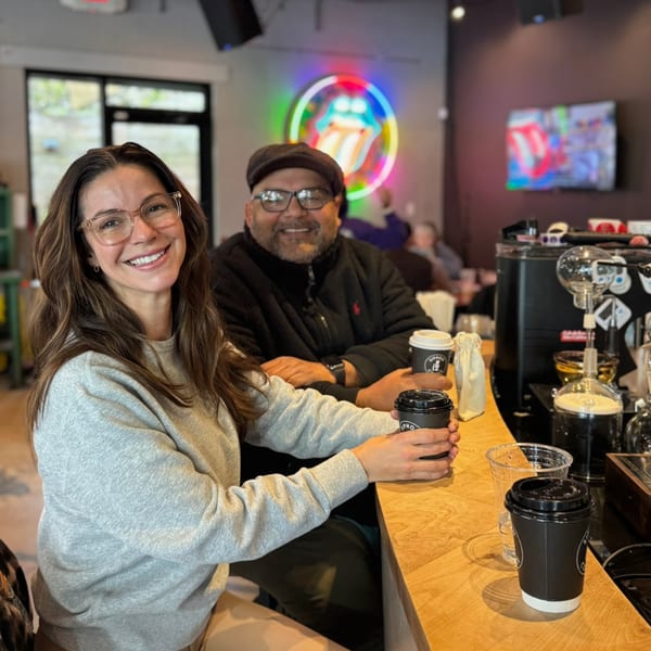 Two smiling people, a woman and a man, sitting at a coffee bar with drinks.