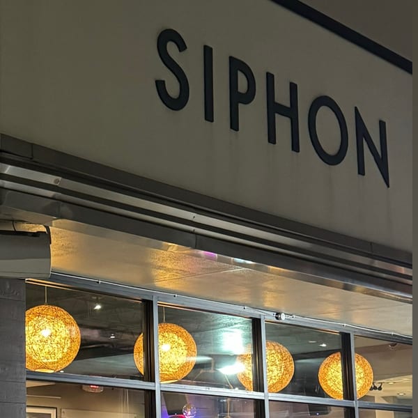 The Siphon restaurant sign above a window displaying four glowing, spherical, woven light fixtures.