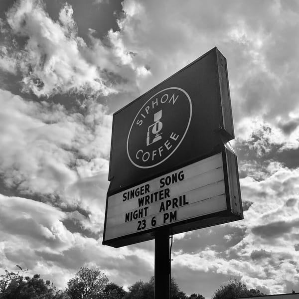 Black and white photo of a Siphon Coffee sign advertising a Singer Songwriter Night on April 23.