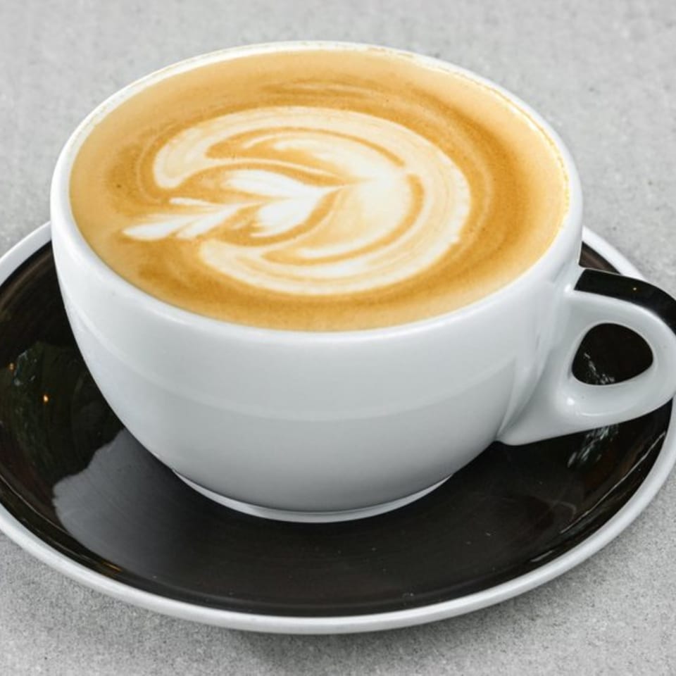 A white cup of latte with a leaf design in the foam, sitting on a black saucer.