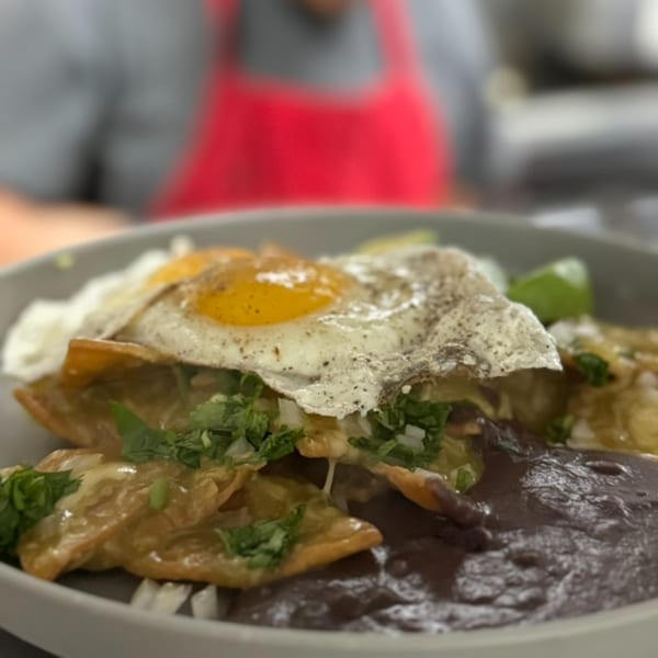 Chilaquiles with fried eggs, black beans, cilantro, and onions in a gray bowl.