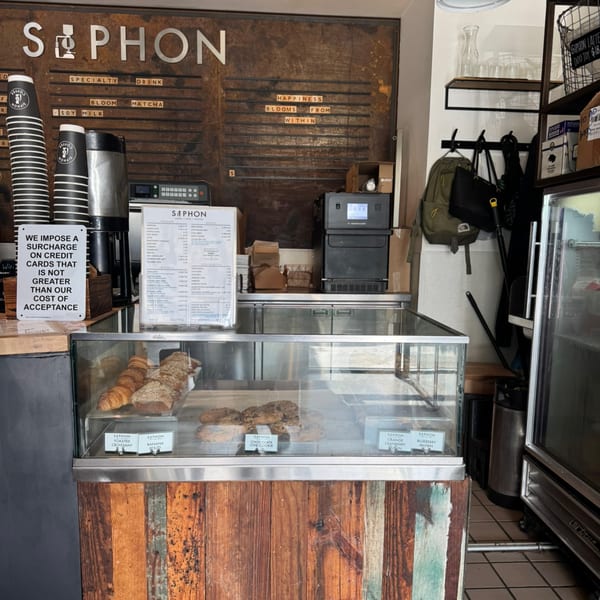 A Siphon coffee shop interior with a pastry display case, menu board, and coffee equipment.