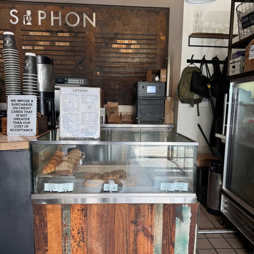 A Siphon coffee shop interior with a pastry display case, menu board, and coffee equipment.