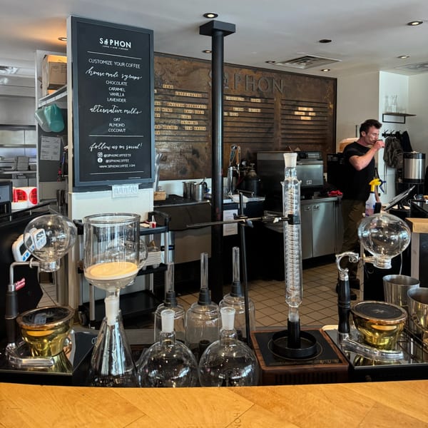A barista works behind a counter with various coffee brewing equipment at Siphon Coffee.
