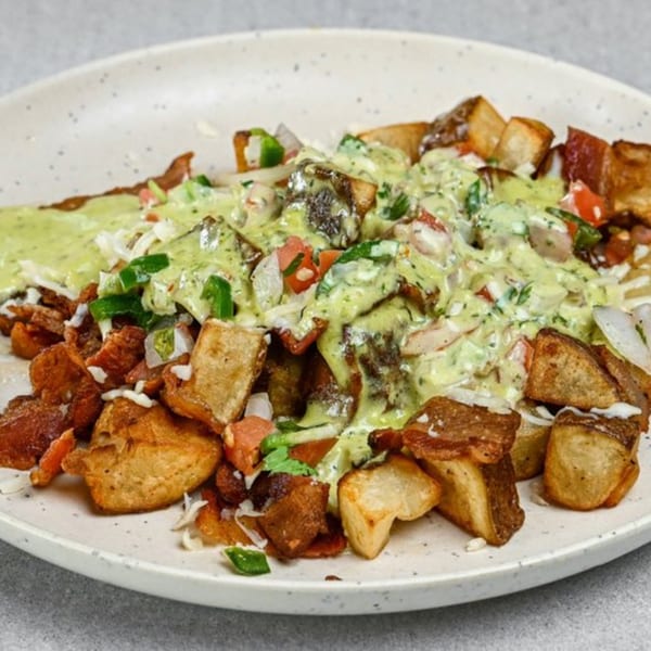 Crispy fried potatoes topped with a creamy green sauce, diced tomatoes, and green peppers on a white plate.