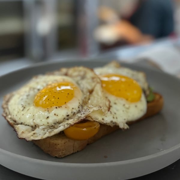 Two fried eggs with runny yolks and pepper on toast with yellow tomatoes on a gray plate.