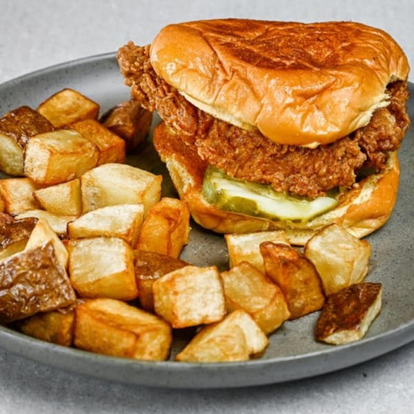 Crispy fried chicken sandwich with pickles on a brioche bun, served with roasted potato cubes.